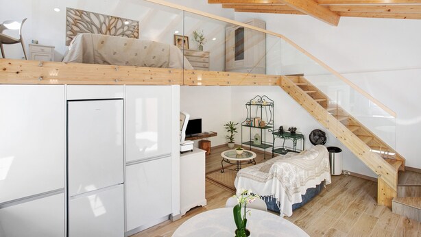 A loft-style bedroom with a wooden ceiling, a glass wall, a bed, a desk, and a small table with a plant. - Zeca Holidays Atalaia Mezzanine Apartment with Balcony and Wi-Fi (Atalaia)