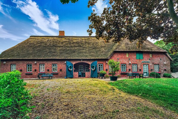 A red brick building with a thatched roof, a green door, and a bench in the foreground.