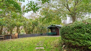 A rustic cabin with a porch, surrounded by a garden with a stone path leading to it.