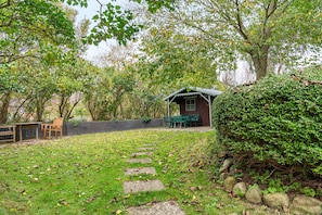 Un chalet rustique doté d’un porche, entouré d’un jardin avec un sentier de pierres menant à l’entrée.