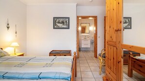 A bedroom with a bed, bedside tables, a wooden wardrobe, a mirror, and a bathroom visible through an open door.