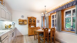 A kitchen with a dining table, chairs, a cabinet, and a window with curtains.