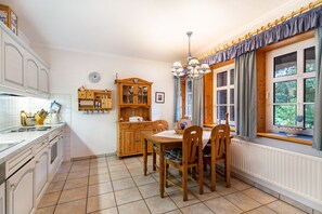 A kitchen with a dining table, chairs, a cabinet, and a window with curtains. - Apartment 'Ferienwohnung Nord-West' with Private Garden and Wi-Fi (Pellworm)