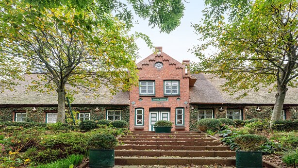 A brick building with a symmetrical facade, a central entrance, and steps leading up to it.