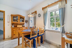 A dining area with a wooden table and chairs, a cabinet with dishes, and a window with curtains.