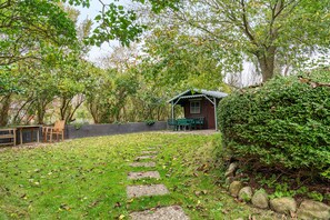 A rustic cabin with a porch, surrounded by a garden with a stone path leading to it.