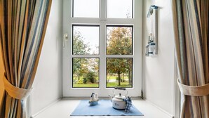 A window with a view of trees and a white wall with a clock. - Apartment 'Ferienwohnung Süd-West' with Private Garden and Wi-Fi (Pellworm)