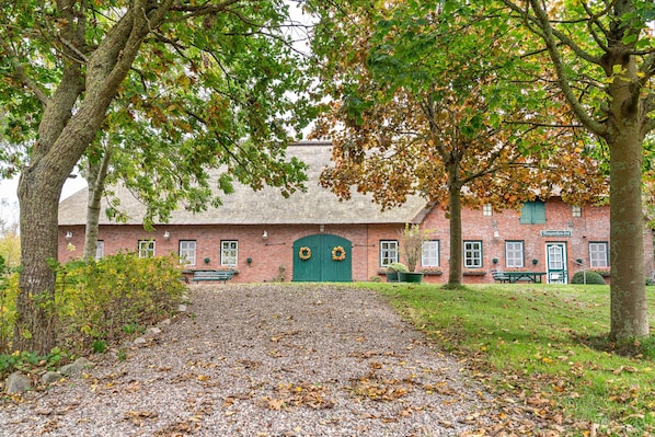 A brick building with a green door, a gravel path, and trees.