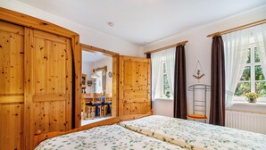 A bedroom with a wooden wardrobe, a bed with floral bedding, a window with curtains, and a view of a dining area. - Apartment 'Ferienwohnung Süd-West' with Private Garden and Wi-Fi (Pellworm)
