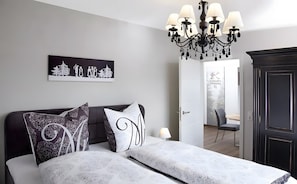 A bedroom with a bed, a chandelier, a door with a deer decal, and a painting on the wall.