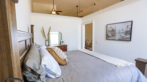 A bedroom with a large bed, a wooden headboard, a ceiling fan, a nightstand with a lamp, and a framed picture on the wall. - Lookout Loft over the Monroe Square (Monroe)