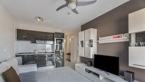 Ein modernes Wohnzimmer mit Fernseher, einer Couch und einer Küche im Hintergrund.