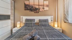 Ein Schlafzimmer mit einem Bett, zwei Nachttischen, einem Wandbild und einem Fenster mit Vorhängen.