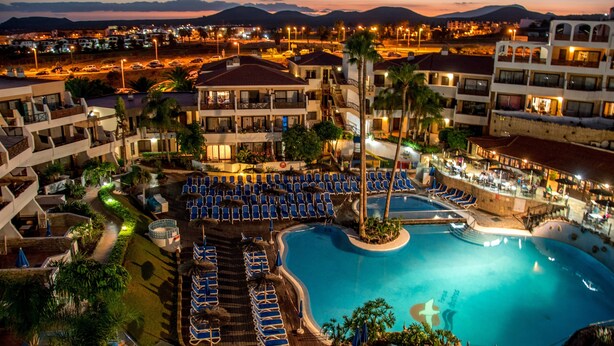 Ein Resort mit großem Pool, mehreren Liegebereichen und Blick auf die nächtliche Skyline.