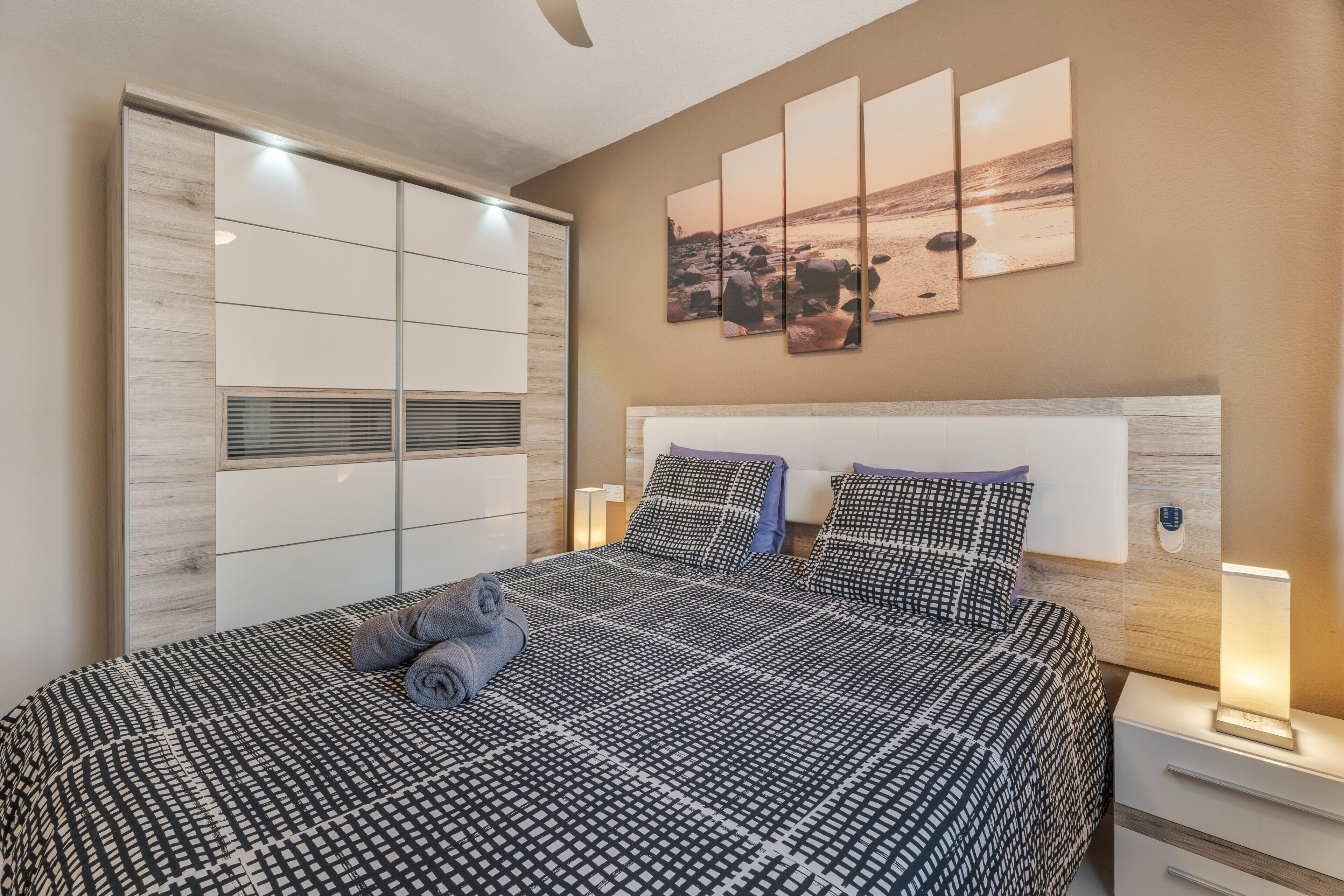 Un dormitorio con cama, mesitas de noche, un armario y una obra de arte en la pared.