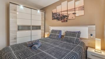Un dormitorio con cama, mesitas de noche, un armario y una obra de arte en la pared.