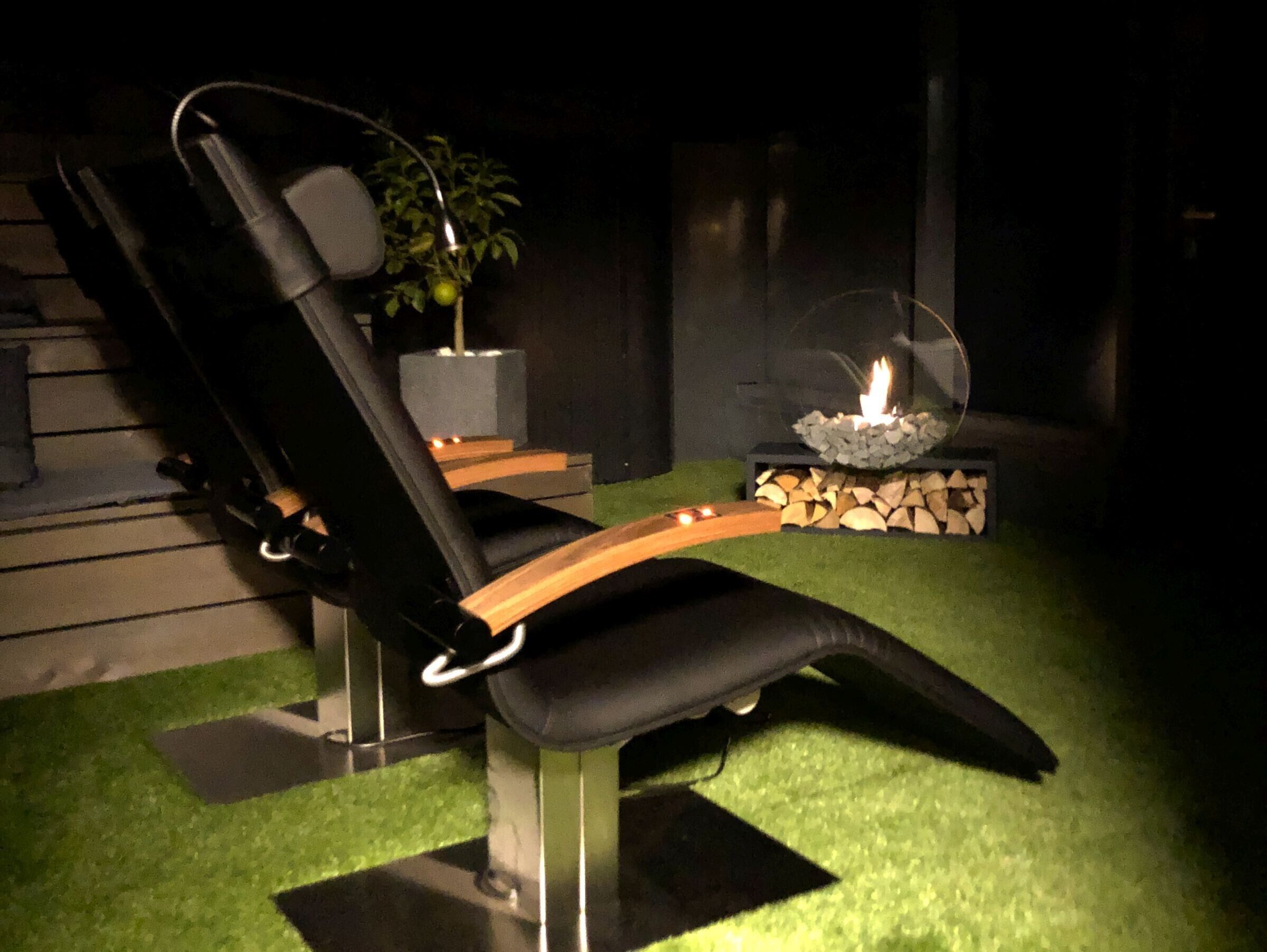A reclining chair with a wooden armrest, a potted plant, and a fire feature.