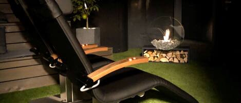 A reclining chair with a wooden armrest, a potted plant, and a fire feature.