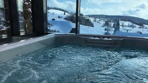 A hot tub with a view of a snowy landscape through large windows. - Apartment 'Halali' with Spa Area and Mountain View (Ibach)