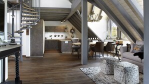 A spacious loft with a wooden staircase, a kitchen with a central island, and a cozy seating area with ottomans. - Apartment 'Halali' with Spa Area and Mountain View (Ibach)