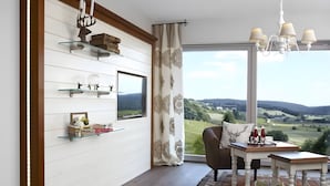 A modern living room with a large window, a dining area, and a TV mounted on the wall. - Apartment 'Kuckucks' with Spa Area and Mountain View (Ibach)