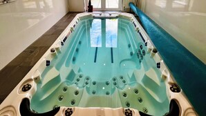 Ett spa-rum med ett stort bubbelbad, en skjutdörr i glas som leder ut till en trädgård och ett tak med dekorativa målningar av fiskar och havsdjur.