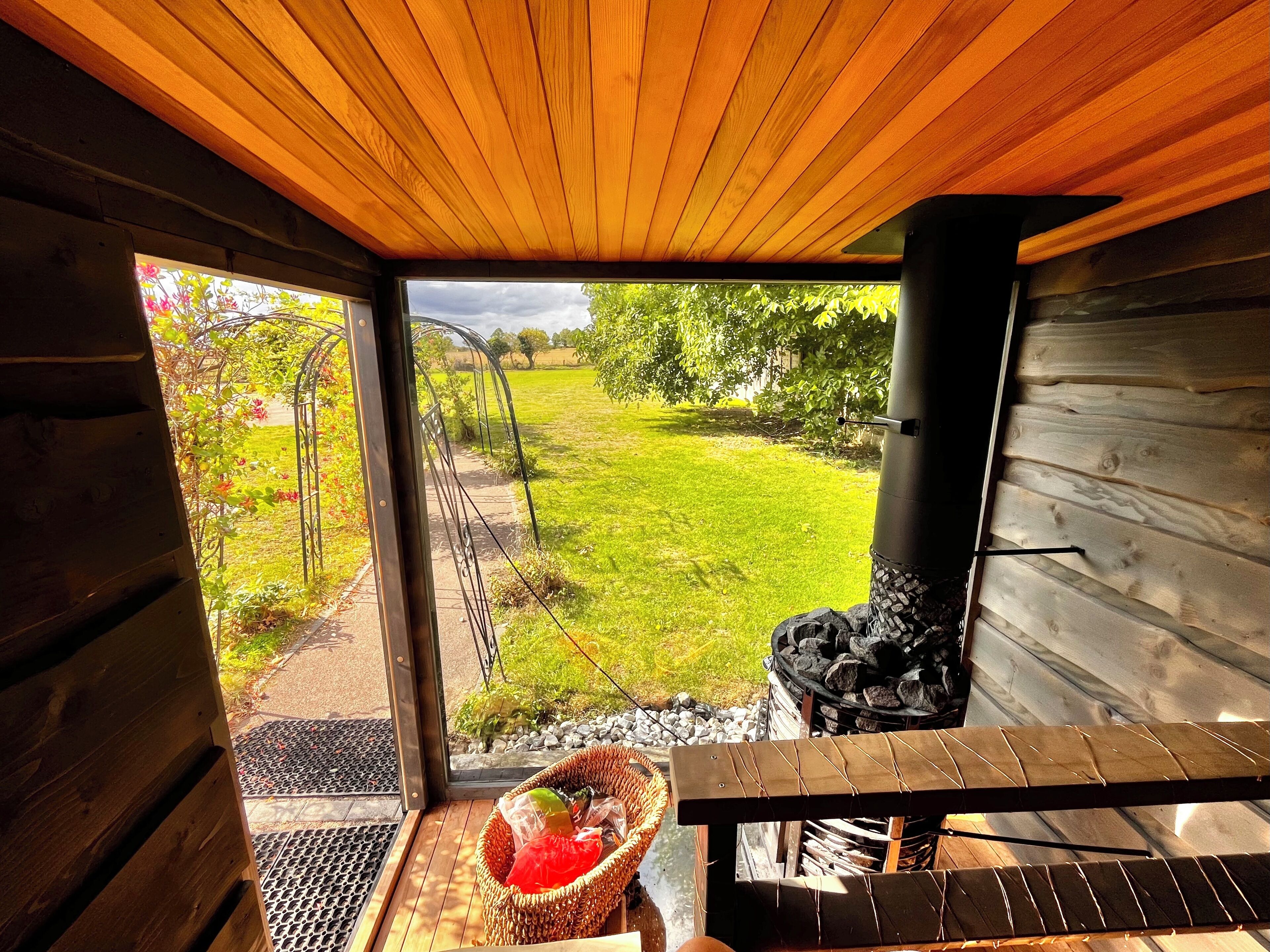A wooden interior with a view of a grassy outdoor area, a metal bench, and a wicker basket with items.