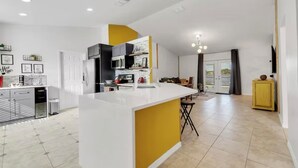 A modern kitchen with a central island, a dining area with chairs, and a yellow cabinet.
