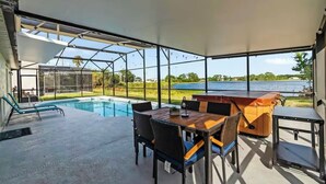 A modern outdoor patio with a pool, dining area, and a view of a lake.