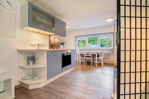Une cuisine moderne avec des meubles gris, un four encastré et un coin repas comprenant une table et des chaises.