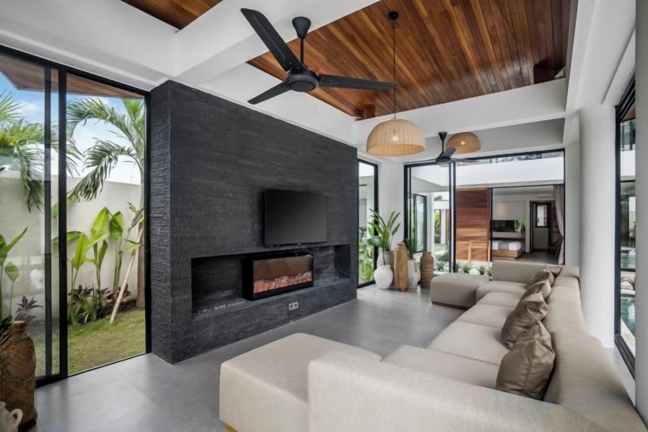 Un salon moderne doté d’une cheminée, d’un ventilateur de plafond et d’une grande fenêtre donnant sur un jardin.
