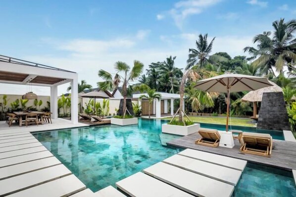 A pool area with lounge chairs, umbrellas, and a pergola structure.