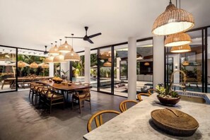 Un comedor amplio con varias mesas y sillas, grandes lámparas colgantes y vistas al exterior.