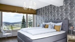 A bedroom with a large bed, a chandelier, a clear chair, and a view of the outdoors. - Apartment 'Chillout' with Spa Area and Mountain View (Ibach)