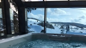 A hot tub with a view of a snowy landscape through large windows. - Apartment 'Chillout' with Spa Area and Mountain View (Ibach)