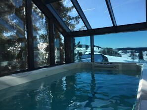Une piscine intérieure donnant sur un paysage enneigé grâce à de grandes fenêtres.
