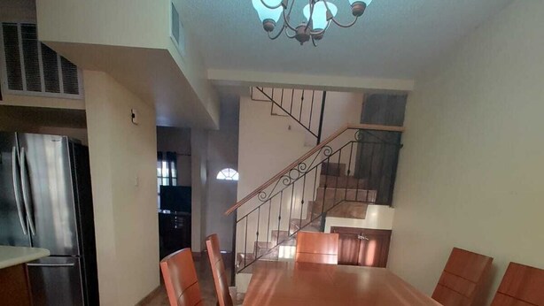 A spacious dining area with a wooden table and chairs, a chandelier, and a staircase leading to an upper level. - House 2121. (Juárez)