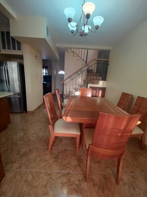 Une salle à manger spacieuse avec une table et des chaises en bois, un lustre et un escalier menant à un niveau supérieur.