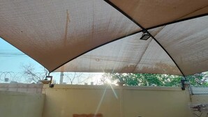 An outdoor patio with a table, a bench, and two chairs under a large canopy. - House 2121. (Juárez)