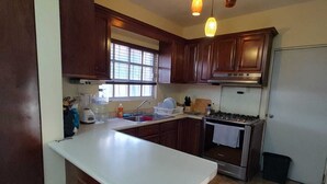 A kitchen with dark wooden cabinets, a white countertop, a stove, and a window. - House 2121. (Juárez)