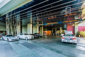 A modern hotel entrance with a glass facade, valet check-in, and a taxi stand.