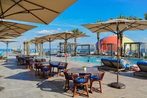 Un espace aménagé au bord de la piscine, avec des chaises longues et des parasols, une piscine et une vue sur l’océan.