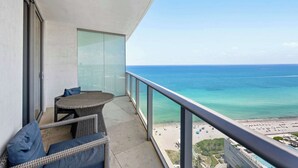A balcony with wicker furniture and a glass door, overlooking a beach and ocean. - Beautiful Hyde Resort Luxe 2BR Private Beachfront (Hollywood)