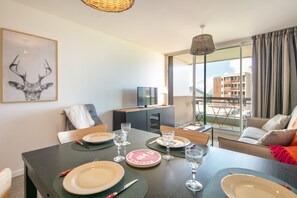 A dining area with a table set for four, a television, and a balcony with a view of buildings and mountains.