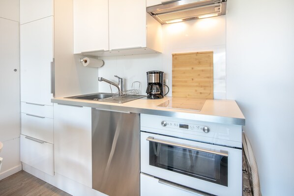 Een moderne keuken met witte kastjes, roestvrijstalen apparatuur, een spoelbak en een koffiezetapparaat.