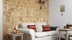 A white sofa with patterned cushions, a small wooden table with a bottle and snacks, and a decorative wall panel. - Apartment 'Hotzenwald' with Spa Area and Mountain View (Ibach)