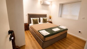 Ein modernes Schlafzimmer mit Bett, Fenster mit Jalousien, Wandklimaanlage und Holzboden.