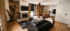 Ein modernes Wohnzimmer mit Kamin, einer schwarzen Ledersofa, einem Esstisch mit Stühlen und einer Küchenzeile mit Schränken und Geräten.