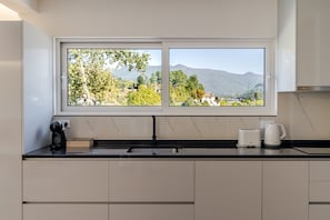 A kitchen with a large window, a sink, a toaster, and a kettle.