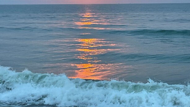 A sunset over the ocean with waves crashing onto the shore.